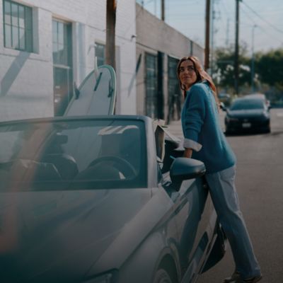 Mujer apoyada en un carro con un saco azul