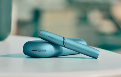 Gros plan sur un appareil IQOS turquoise posé sur une surface claire avec un arrière plan flou.