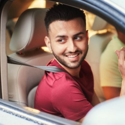 A bearded man wearing headphones holds and IQOS device. 
