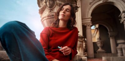 Una mujer sostiene un dispositivo IQOS mientras mira hacia una computadora portátil.