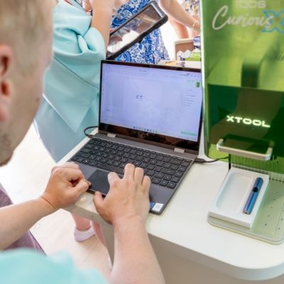 Osoba používa notebook na nastavenie gravírovacieho zariadenia vedľa na podujatí.