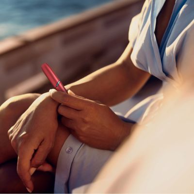 Eine Frau sitz am Wasser und hält einen IQOS Orginal DUO in ihrer Hand