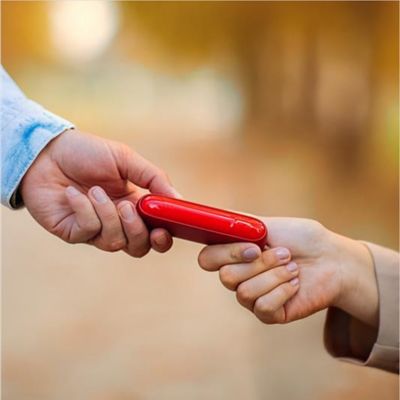 Zwei Personen übergeben sich ein rotes IQOS ORIGINALS DUO Gerät.