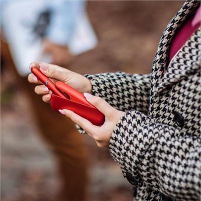 Eine Person nimmt einen roten IQOS ORIGINALS DUO Holder aus dem passenden Pocket Charger.