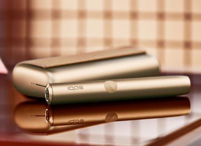 The IQOS ORIGINALS DUO heated tobacco device in silver and three packs of HEERTS tobacco sticks.