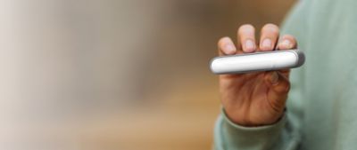 Eine Person präsentiert ein helles IQOS ORIGINALS DUO Gerät vor einem verschwommenen Hintergrund.