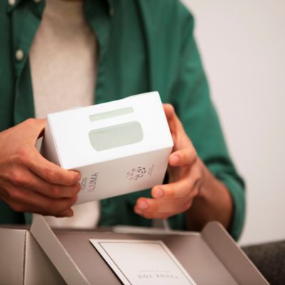 Jemand hält einen Karton mit einem IQOS ILUMA Gerät in der Hand