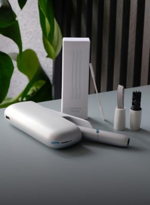 IQOS ORIGINALS DUO Silver liegt neben IQOS-Reinigungstool und Reinigungs-Sticks.