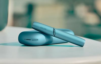 Gold IQOS device, a mobile, a yellow cup and a glass of water on a table bar 