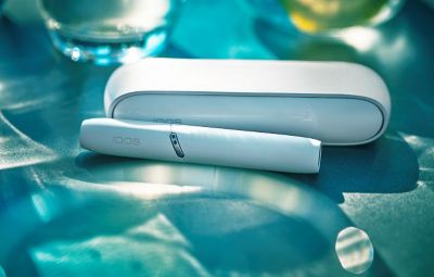 Gold IQOS device, a mobile, a yellow cup and a glass of water on a table bar 