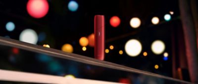 Ein rotes IQOS One steht vor einem schwatzen Hintergrund mit Lichtpunkten