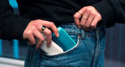 Eine Hand steckt sich zwei IQOS Geräte in die Hosentasche