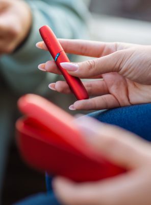 Hände halten ein rotes IQOS ORIGINALS DUO. 