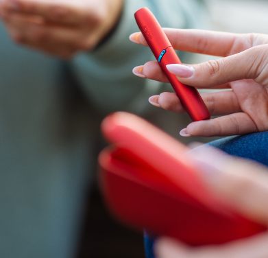Eine weibliche Hand hält den IQOS Duo in rot.