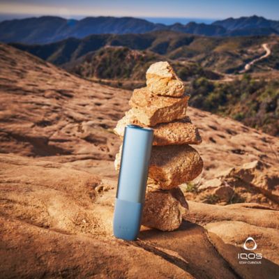 IQOS ILUMA One in front of a stack of rocks by the mountain