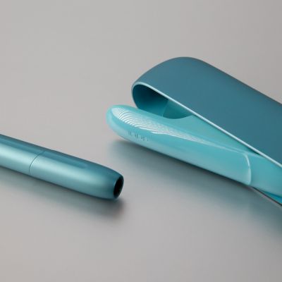 Ein türkises IQOS ORIGINALS DUO Gerät liegt auf einer grauen Oberfläche. 