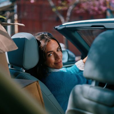 Mujer recargada en asiento trasero de auto usando IQOS Iluma i ONE.