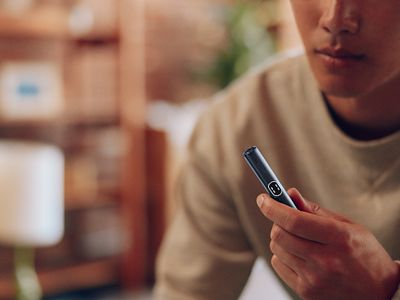 Persona usando IQOS Iluma i turquesa mientras revisa el dispositivo en interior