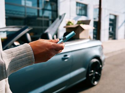 Hombre usando IQOS Iluma i turquesa en exterior junto a automóvil