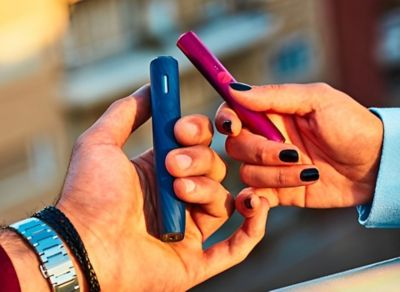 Ruce držící dvě zařízení IQOS 