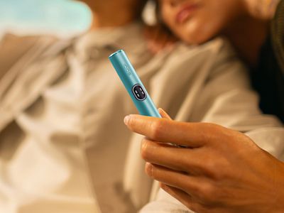 Ruka držící zařízení IQOS ILUMA i v pozadí muž a žena