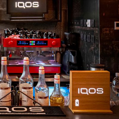 Cedulka IQOS položená na pultě vedle lahví v IQOS Lounge