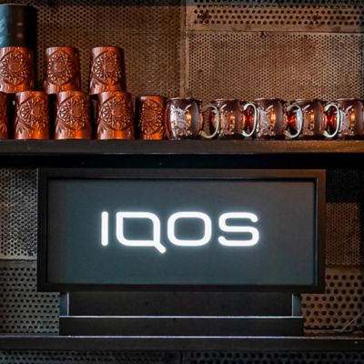 Držák s logem IQOS na pultě vedle hrnků v IQOS Lounge