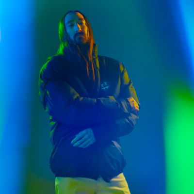 Steve Aoki oblečen v limitované edici bundy IQOS x STEVE AOKI na barevném pozadí.