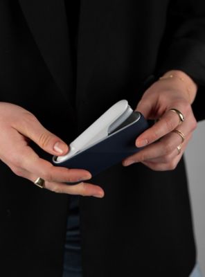 Nahaufnahme von Händen, die einen silbernen IQOS-Holder aus einem dunkelblauen Charger entnehmen. 