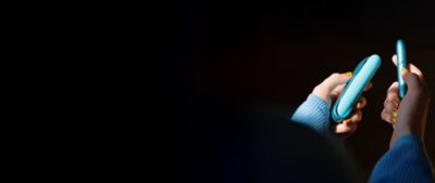 Close-Up zweier Hände, die das IQOS ORIGINALS DUO Turquoise vor einem dunklen Hintergrund halten. 