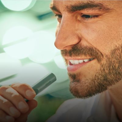 Un hombre sonriente sosteniendo un dispositivo IQOS ILUMA Moss Green.