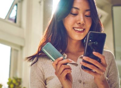 Woman using smartphone and holding IQOS Iluma device