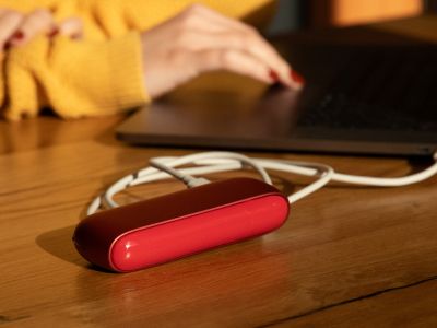IQOS ORIGINALS DUO Scarlet per Kabel mit Laptop verbunden, Person tippt im Hintergrund.