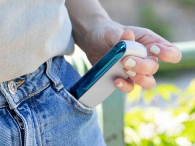 Hand steckt IQOS ORIGINALS DUO Silver mit blauem Klappen-Cover in Jeans-Tasche.