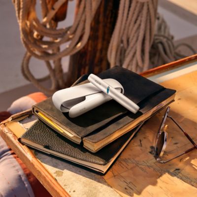 Lifestyle Bild eines IQOS ORIGINALS DUO Silver, platziert auf einem Stapel von Notizbüchern. 