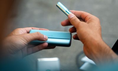 A smiling woman with an IQOS ILUMA device.