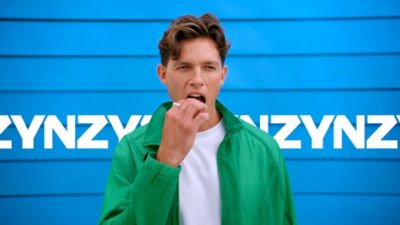 Muž v bílém tričku a zelené košili dávající si nikotinový sáček ZYN do pusy