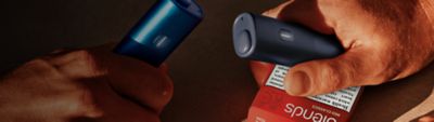 one hands: one holding a black BONDS 2 by IQOS device and a BLENDS Red Classics pack