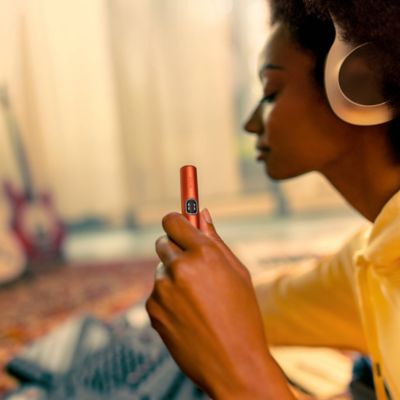 Person indoors wearing headphones and holding an ILUMA i holder, with a warm, blurred background creating a relaxed atmosphere.