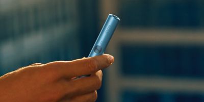 جهاز IQOS ILUMA i PRIME باللون النبيتي فوق شاحنه