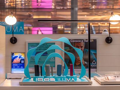 Vitrina IQOS ILUMA con dispositivos en diferentes colores sobre base turquesa.