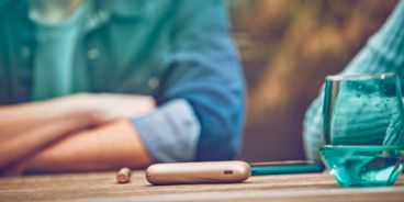 EIn IQOS DUO liegt auf einem Tisch, im Hintergrund sitzen Personen