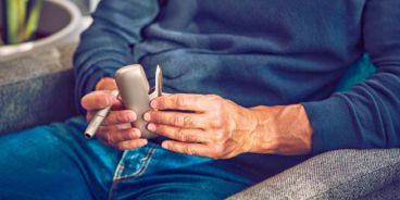 Eine Person hält ein IQOS in der Hand und sitzt dabei