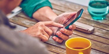 Eine Person ist am Handy, daneben liegt ein IQOS Gerät