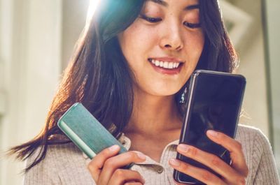 Usmívající se žena drží mobilní telefon a zařízení IQOS.