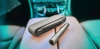 A woman holding an IQOS device looking at a laptop.