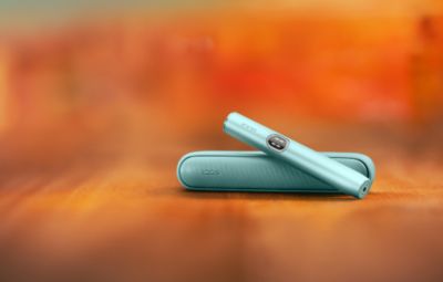 Appareil IQOS ILUMA i couleur aigue-marine (appareil tout-en-un) posé sur un fond dégradé orange