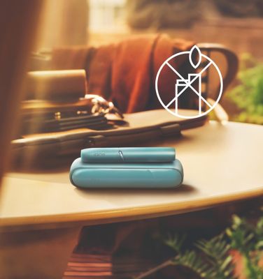 Ein blaues IQOS ORIGINALS DUO Gerät liegt auf einem Tisch vor einem Symbol mit durchgestrichenem Feuerzeug.