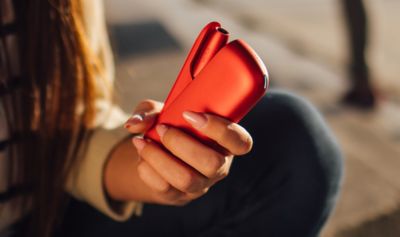 Person hält ein geöffnetes IQOS ORIGINALS DUO Scarlet in Hand.