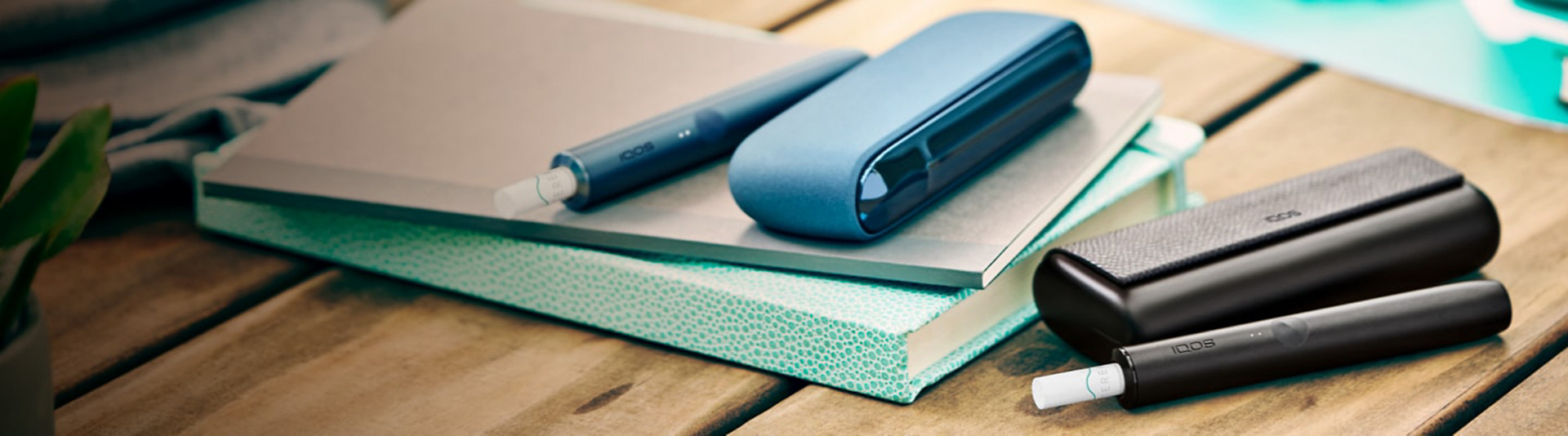 Two iqos ILUMA Devices resting on a wooden table, one of which rests on a blue notebook